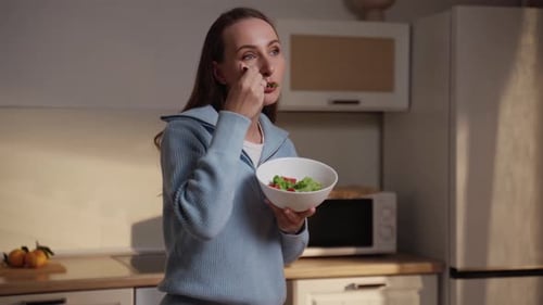 Young Brunette Woman in a Blue Sweater Eats a Healthy Salad Made From Fresh Green Ingredients