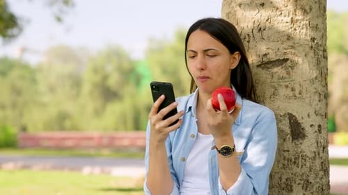 Woman Relaxes with Apple and Phone by Tree