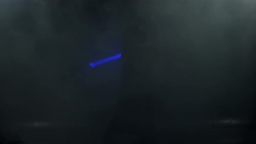 Young Man in Jedi Cosplay Costume with Lightsaber Battle on Black Background in Smoke and Rain Slow