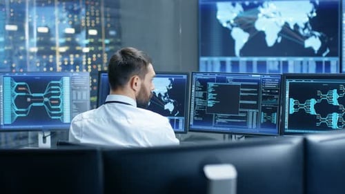 Vista posterior del operador del centro de control del sistema trabajando. Varias pantallas que muestran datos técnicos.