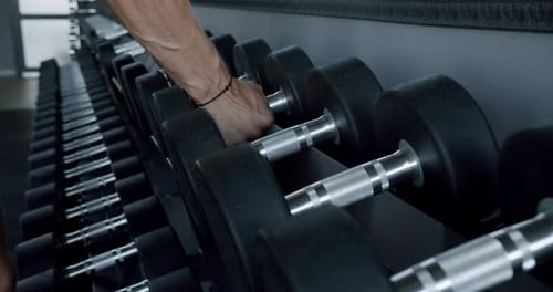 Closeup of Male Hand Take Iron Dumbbells From Rack for Workout at Gym