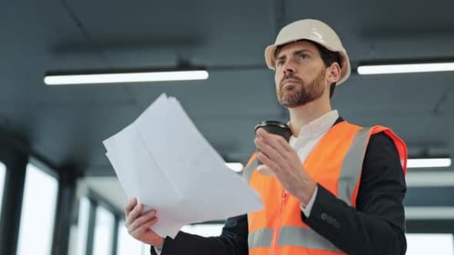 Focused Architect Reviews Blueprints with Coffee at Construction Site
