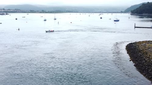 Motorboat aerial view leaving Welsh seaside town harbour cruising along River Conwy