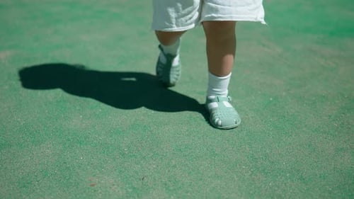 Legs of infant baby girl walking on a green Badminton court outdoors - slow motion