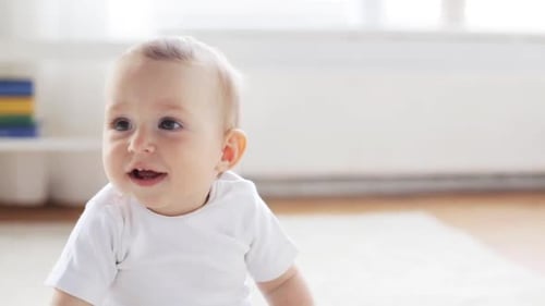 Happy little baby sitting on floor in bright living room at home