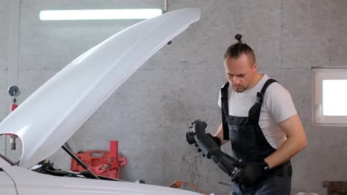 A Man Working Under an Open Hood of a Vehicle in a Garage