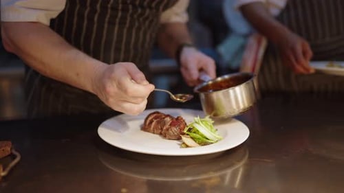 View of a chefs hand pouring sauce over meat in a fine dining restaurant