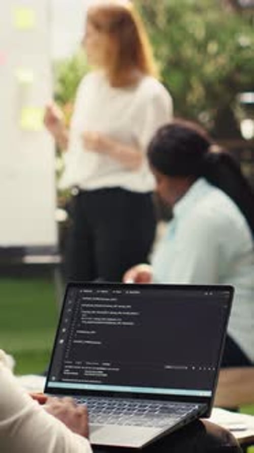 Developer Coding on Laptop During a Business Meeting in Modern Office