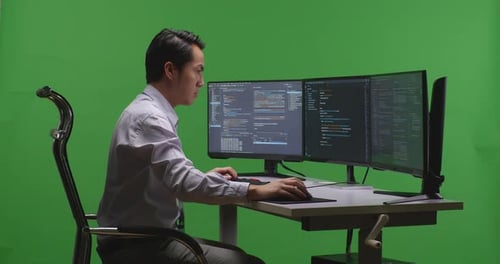 Asian Man Developer Using Computer To Write Code With Multiple Screens In Green Screen Studio
