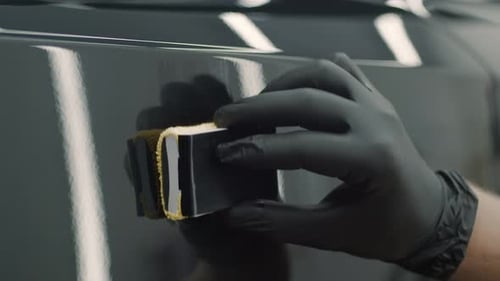 Closeup of Car Wash Workers Applying Wax with Sponge to Body of Black Automobile Indoor Worker