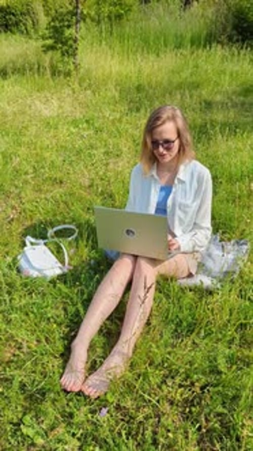 Woman Works on Laptop in Grassy Field