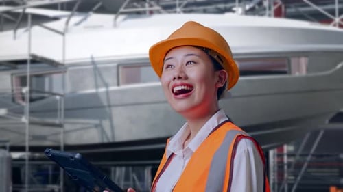 Side View Of Asian Female Engineer Looking At The Tablet In Her Hand in Modern Shipyard