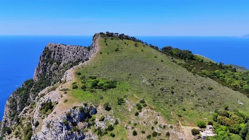 Stunning coastal landscape showcases a rocky hillside meeting the clear blue sea under bright sunlig