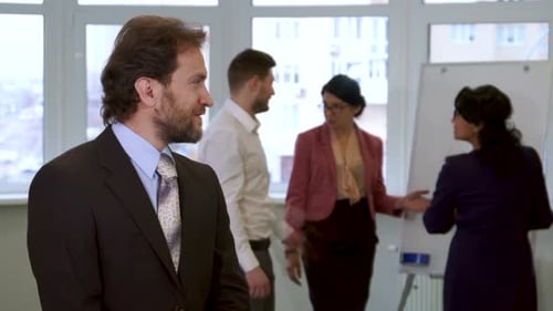 Confident Businessman Poses While Colleagues Collaborate in the Office