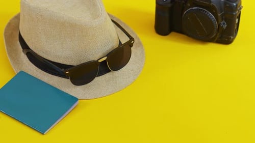 Travel flat lay with straw hat, sunglasses, vintage camera, and passport on yellow background
