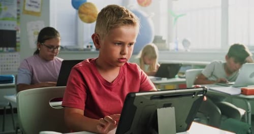 Elementary School Boy Sitting at Desk Using Digital Tablet Studying Basic Programming