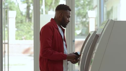 NEW YORK April 5 2018 Profile of Focused Young African Man in Red Shirt Withdrawing Money From Bank