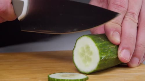 The Hands of a Man Cut a Cucumber with a Knife on a Board