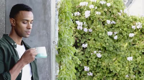 Young Adult Man Drinks Coffee by Floral Garden Wall