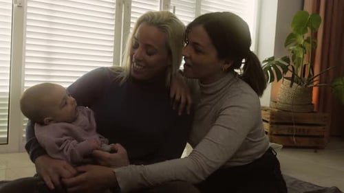 Two Women Smile at Baby Indoors