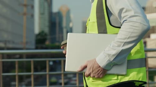 Man Construction Worker Holds Cup of Coffee and Laptop