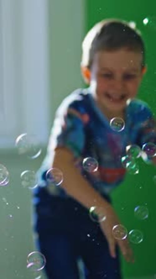 Boy play with bubbles. Cute male child catches soap bubbles at home Vertical video