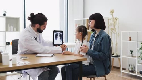 Caucasian Doctor Explains Xray Results to Mother and Daughter in Clinic