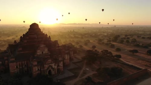 Ancient Buddhist temple in Bagan, Myanmar with dozens of hot air balloons in background during sunri