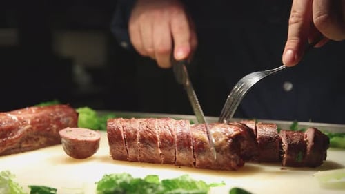 Chef Slicing Cooked Meat Roll with Fork and Knife
