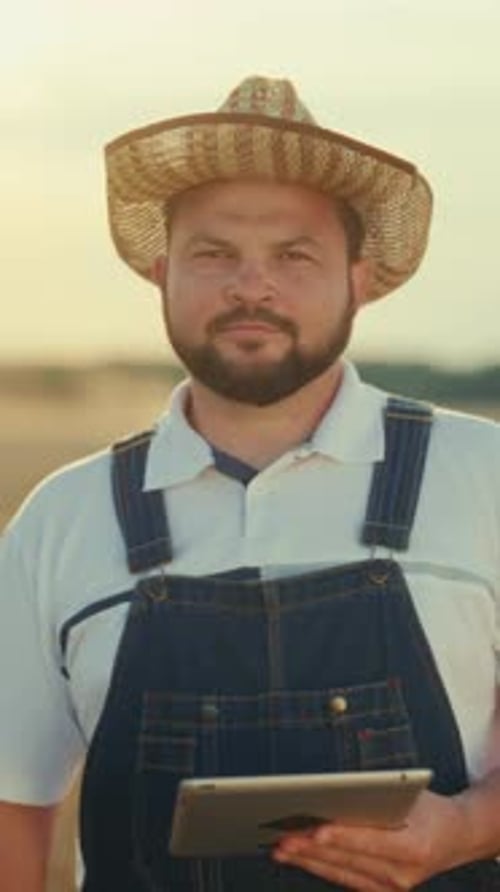 Farmer in Overalls Holding Tablet in Golden Field
