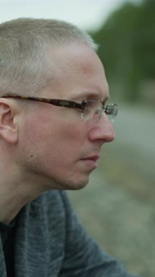Contemplative Man in Glasses Sitting By Railway Track in Serene Forest