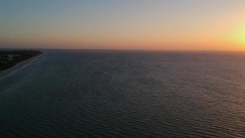 Flying over the waves at Sanibel Island looking down the beach to lighthouse point.