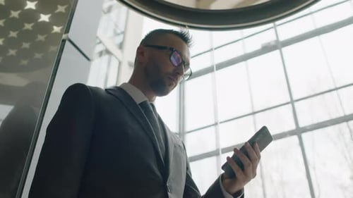 Executive Going up in Panoramic Lift with Cell Phone in Hand