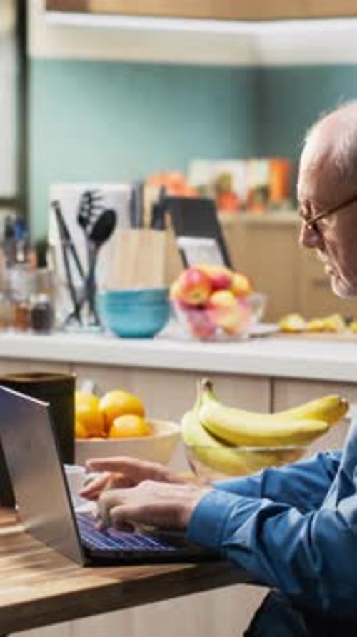 Senior Man Uses Laptop in Bright Kitchen