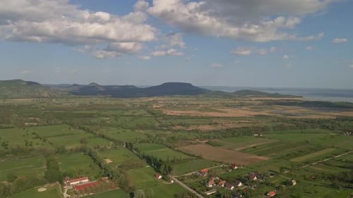 An aerial view of a rural countryside with green fields, small villages, and a large lake in the bac