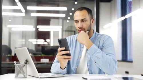 Focused serious African American businessman uses mobile phone at a workplace in a business office.