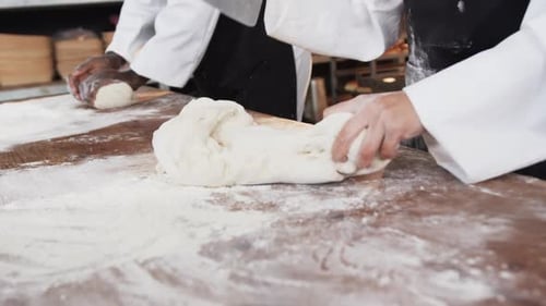 Diverse bakers working in bakery kitchen, kneading dough on counter in slow motion