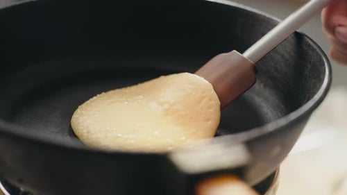 Person Flipping Pancake in Pan with Spatula