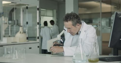 Mature Man Works with Microscope in Research Lab