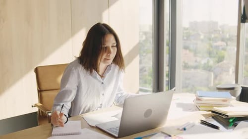 Businesswoman Working in the Office with Important Documents and Laptop Writes Data to Notepad Girl