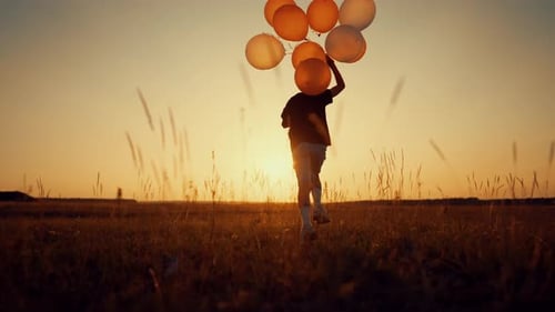 Happy Child Running Over Field with Balloons in Hand Back View Childhood Beautiful Sunset in Nature
