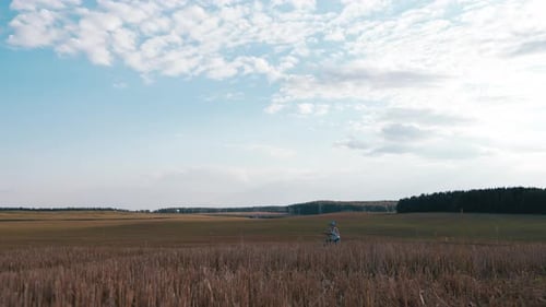 Teen Boy with a Bicycle Walks Along a Mowed Field on a Hill in the Evening Static Shot