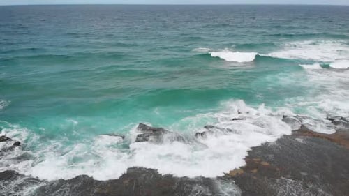 Aerial view of waves crashing over the rocks on a beach located on a tropical island.
