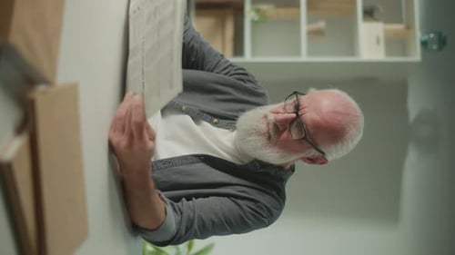 Senior Man Reading Newspaper Indoors Vertically