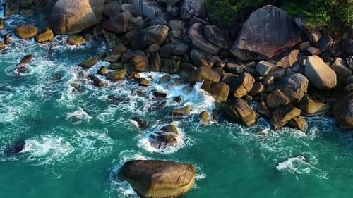 Aerial drone view of foamy waves breaking on a rocky shore.