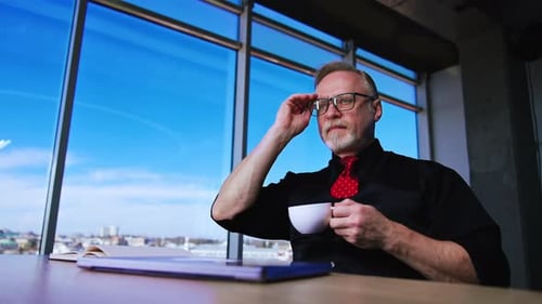 Calm confident Caucasian mature businessman sits at desk in office with cup in hand.