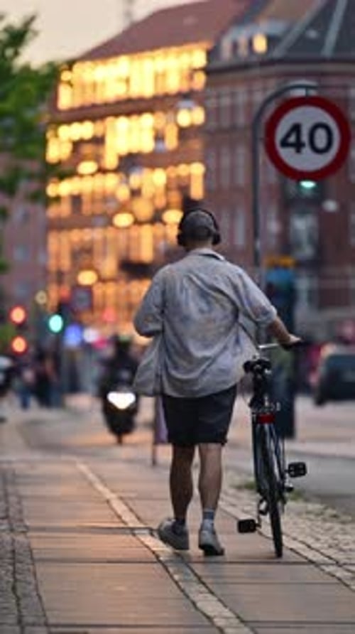 Person walking a bicycle on an urban sidewalk during sunset, enjoying sustainable urban mobility. Co