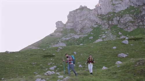 Mountain trail hikers wearing backpacks and carrying trekking poles walking along scenic mountainsid