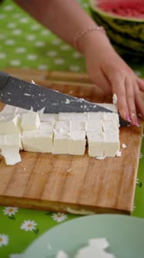 Femme découpant le fromage feta en cubes sur une planche de bois