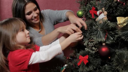 Mother Helps Her Daughter Hang a Beautiful Bauble on the Christmas Tree